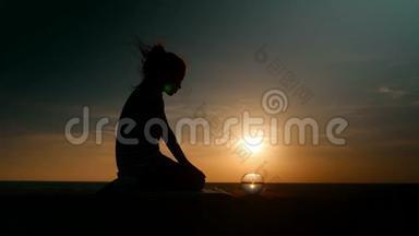 剪影小女孩在日落时的海景背景下，看着小水族馆看着打架的鱼。 概念放松